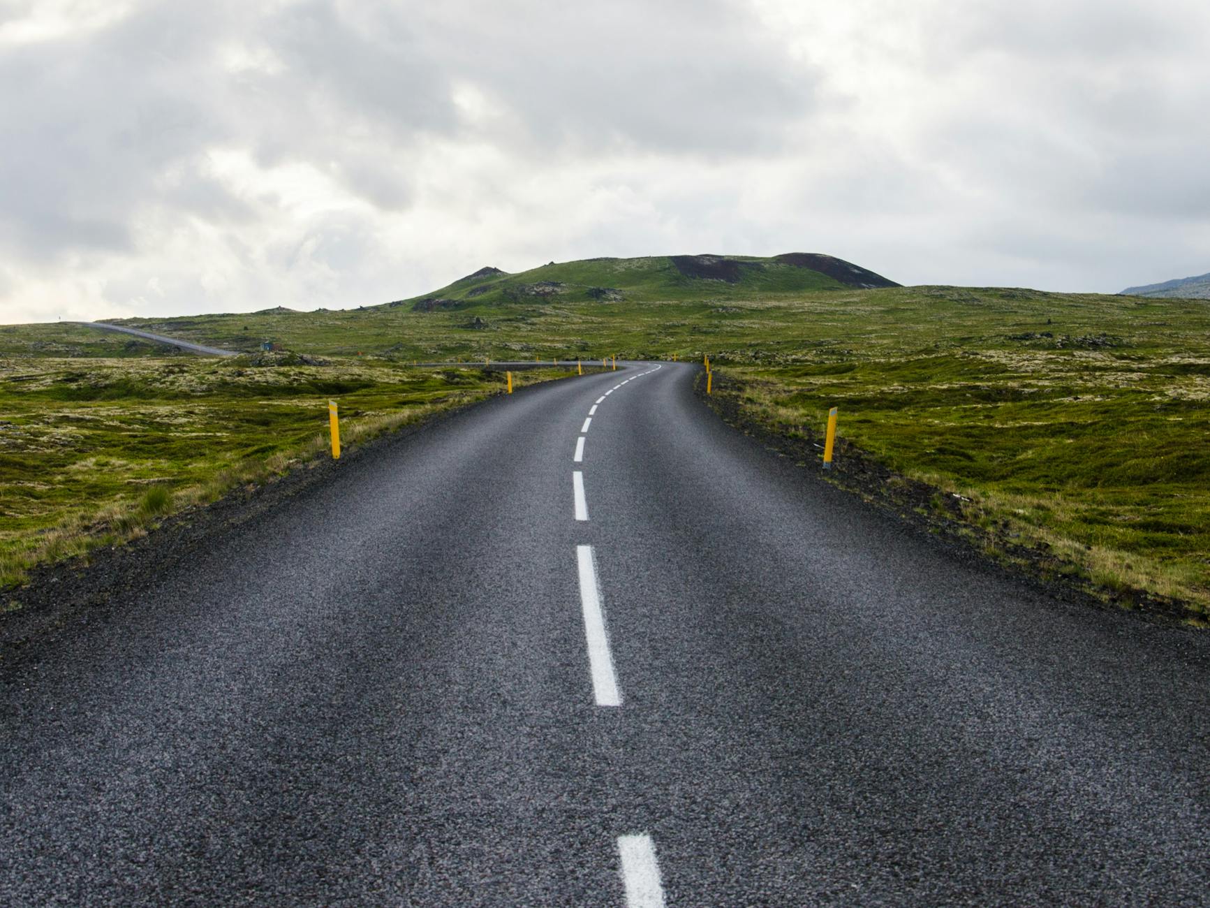 gray concrete road towards green mountain